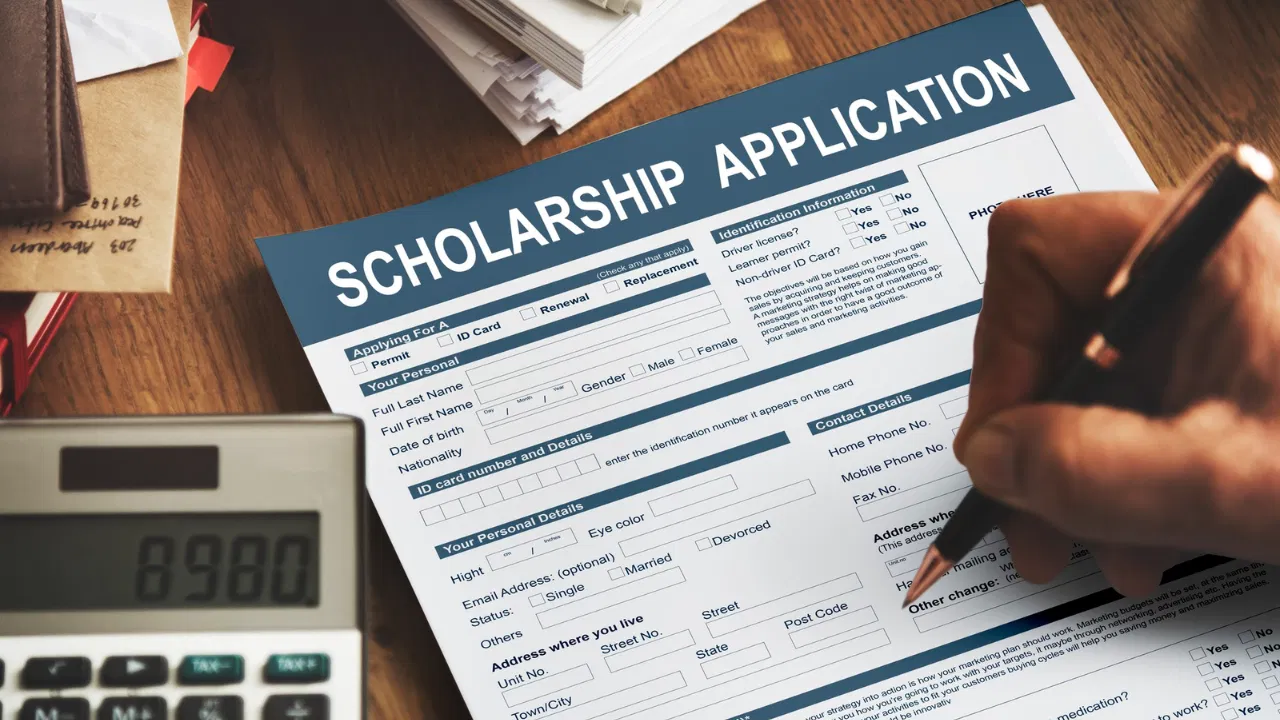 Student filling out CBSE scholarship application form with calculator and documents on the desk