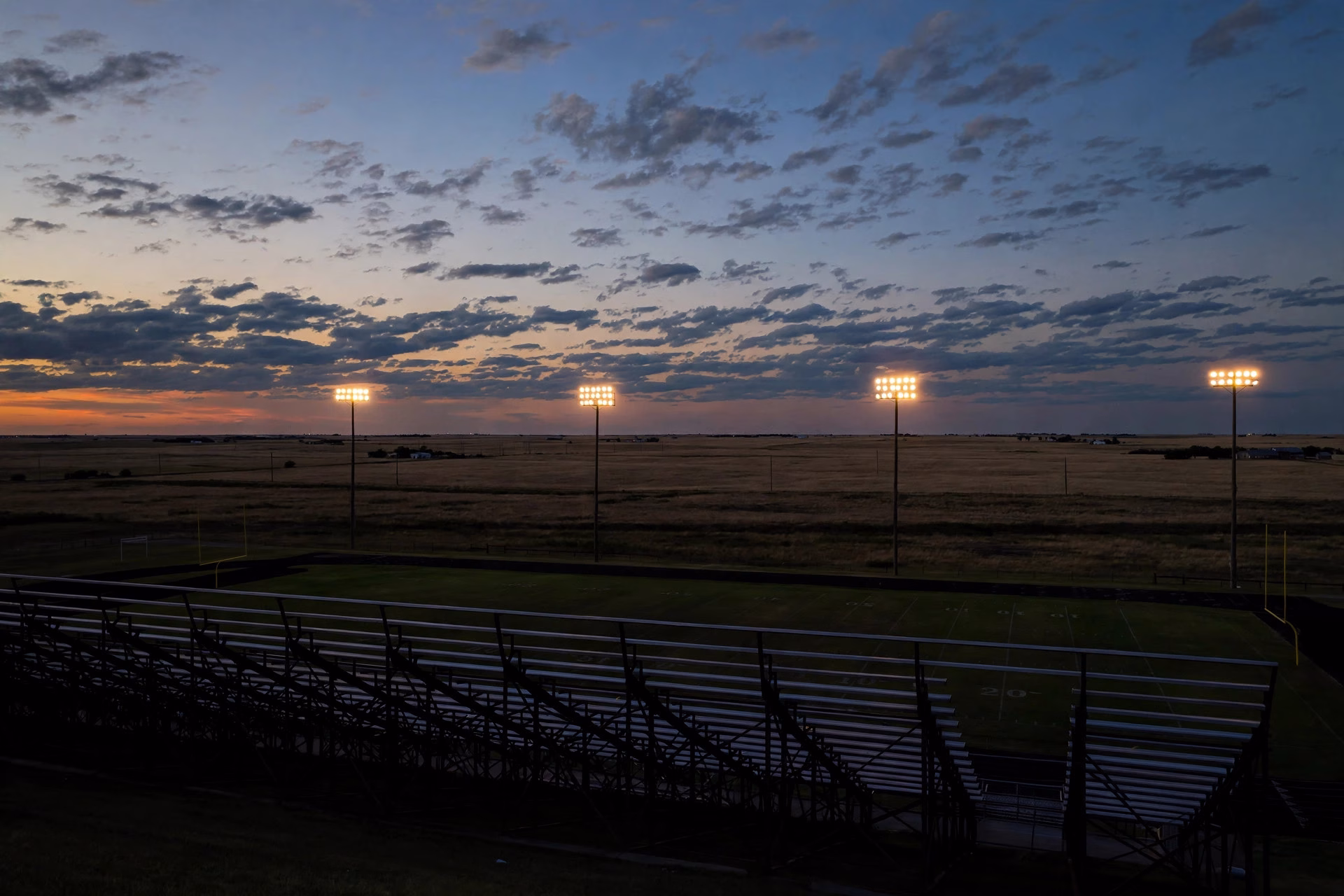 Empty bleachers silhouette at dusk in a small-town Oklahoma football stadium.